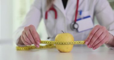 Kadın doktor beyaz masadaki bantlı elmayı ölçer. Kadın beslenme uzmanı sağlık merkezinde kilo kaybı için sağlıklı besin sunuyor