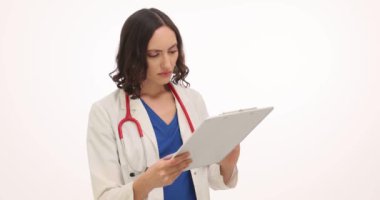 Genç bayan doktor, beyaz arka plandaki tıbbi kayıtları titizlikle inceliyor. Yoğunlaştırılmış hekim randevuda yapılacak konsültasyona hazırlanıyor