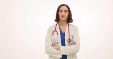 Kadın doktor kollarını kavuşturur ve beyaz arka planda kendine güvenen pozlar verir. Esmer doktor, tıbbi üniformalı fotoğraf için özgüvenle poz veriyor.