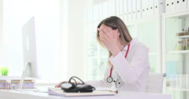 Kadın doktor, klinikteki iş yerinde hastaya danışarak yaptığı jestlerle keyif veriyor. Mutlu kadın doktor sandalyeye yaslanarak güler.