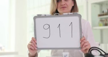 Kadın doktor hastanedeki iş yerinde üzerinde 911 işareti olan beyaz tahtayı tutuyor. Steteskoplu kadın sıhhiyeci telefon numarasını hatırlattı