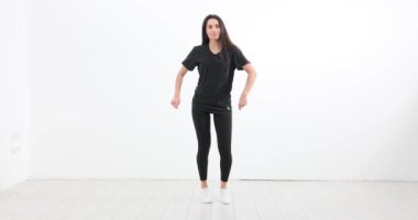 Spor kıyafetlerindeki gülümseyen kadın dans stüdyosunda yeni koreografi çalışması yapıyor. Genç bayan dansçı aktif egzersiz yapar. Yavaş çekim tekniğini geliştirir.