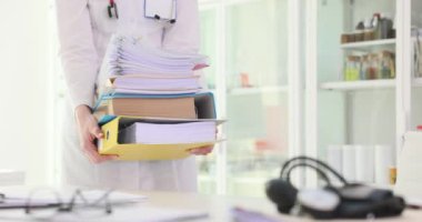 Kadın doktor, hastanedeki masanın üzerine yığılmış klasörler taşıyor. Üniformalı kadın doktor evrak işleri için tıbbi belgeler hazırlıyor.