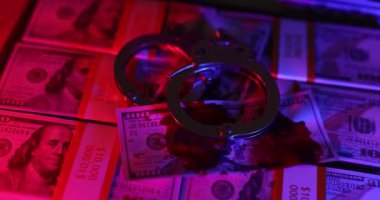 Çelik kelepçeler, kırmızı ve mavi ışıklarla aydınlatılan 100 dolarlık banknotların üzerine yerleştirilmiş. Yasalara aykırı haksız iş kavramı
