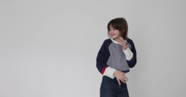 Gülümseyen küçük kız beyaz arka planda günlük kıyafetlerini gösteriyor. Kazağında doğum lekesi olan şirin bir çocuk modeli olumlu duygular ifade eder.