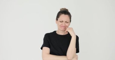 Kadın beyaz arka planda hüzün ve endişe dolu yanaklar taşıyor. Kadın yüzüne dokunur, yalnızlık ve umutsuzluğun derin duygularını ifade eder.