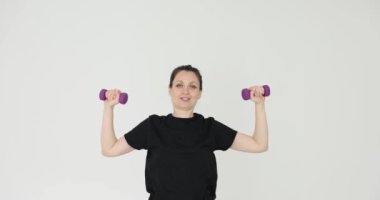 Siyah spor kıyafetleri giyen beden eğitimi hocası beyaz arka planda halter egzersizleri gösteriyor. Mutlu kadın sağlıklı bir hayat sürüyor.