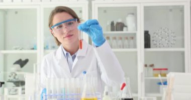 Beyaz önlüklü kadın bilim adamı laboratuarda kırmızı sıvıyla cam tüp tutuyor. Güvenlik gözlüklü kadın işçi çözümü inceliyor