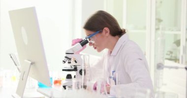 Esmer biyolog, mikroskobu ayarlıyor. İş yerindeki bilgisayardaki verileri yavaş çekimde analiz ediyor. Kadın sağlık sektöründe önemli tıbbi araştırmalar yapıyor.