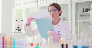 Gözlüklü bir biyolog laboratuarda masa başında otururken raporun sayfalarını çeviriyor. Kadın bilim adamı test sonuçlarını kontrol ediyor. Laboratuvarda çalışmaya hazırlanıyor.