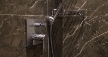 Su damlacıkları krom duş başlığından mermer döşeme duvarına düşer. Gösterişli tasarım ve modern estetik lüks ve rahatlama hissi için.