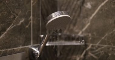 Banyodaki mermer fayanslarla süslenmiş duş başlığından su dökülüyor. Lüks kabinde yıkanan ceset için temiz sıvı akışı.