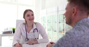 Neşeli doktor, erkek hastayı klinikte ağır çekimde hastalığın belirtilerini anlatırken dinliyor. Arkadaş canlısı terapist randevusunda ziyaretçiyle iletişim kurar.