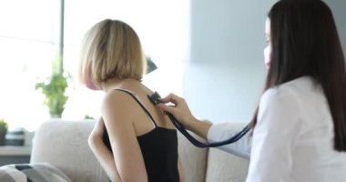 Doktor, evde steteskoplu genç sarışın bir kadının ciğerlerine bakıyor. Öksüren kadın randevusunda terapistle birlikte tıbbi muayeneden geçer.