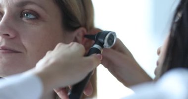Kadın doktor otoskop kullanarak kadın kulak muayenesi yapıyor. Üniformalı özenli sıhhiyeci randevuda organ aramasını kontrol ediyor.