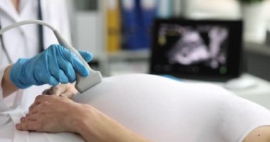 Hamile kadın özel klinikte ultrason muayenesinden geçiyor. Eldivendeki sıhhiye, gelecekteki bebeğin sağlığını randevuda kontrol etmek için dönüştürücü kullanıyor