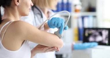 Doktor kadın hastanın dirseğini kontrol etmek için ultrason cihazı kullanıyor. Üniformalı doktor hastanede akut ağrı kaynağı arıyor.