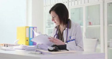 Kadın aile doktoru masasında oturan tıbbi kayıtları inceliyor. Konsantre doktor, hastanın tedavi planını analiz eder ve laboratuvar sonuçlarını kontrol eder.