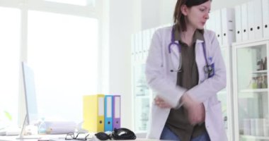 Kadın endişeyle ofiste elini kolunu sallayarak dolaşıyor. Kadın doktor bilgisayardaki tıbbi geçmişleri inceleyerek karmaşık teşhisler koyuyor.