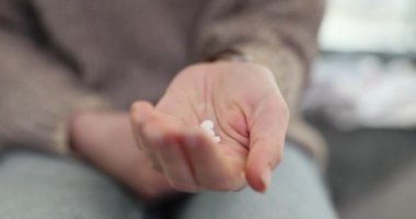 Kadın koltukta oturmuş elindeki haplara dikkatlice bakıyor. Evde tedavi gören bir avuç dolusu yuvarlak uyuşturucuyu sıkan bir kadın.