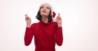 Noel Baba şapkası takan esmer kadın beyaz arka planda şans diliyor. Kırmızı elbiseli kadın başını kaldırıp Noel mucizesinin yavaş çekimde olmasını umuyor.