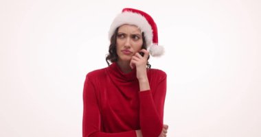 Kırmızı Noel şapkalı düşünceli kadın beyaz duvarda sorun çözme arayışında. Genç bir kadın ağzını açar işaret parmağını kaldırır.