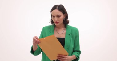 Yeşil ceketli iş kadını beyaz arka planda kahverengi zarfı açıyor. Şok olmuş genç bir kadın, iş mektuplarını okurken şaşkınlık içinde.