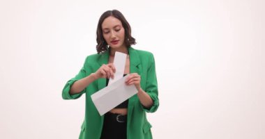 İş kadını mektubu beyaz arka planda zarfa koyar. Yeşil ceketli, dost canlısı gülümseyen esmer kadın mesajı okumayı teklif ediyor.