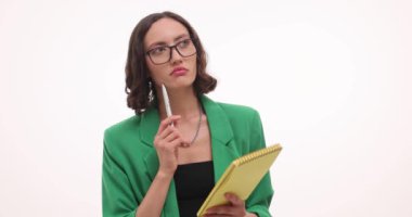 Yeşil ceketli düşünceli bir iş kadını beyaz üzerine not defterine not alır. Odaklanmış genç dişiler gelecekteki iş görevleri hakkında yazılar yazıyor.