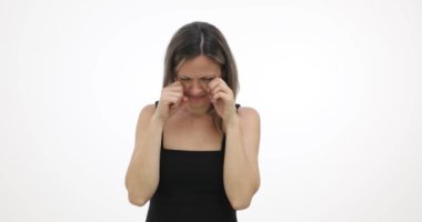 Üzgün sarışın kadın gözyaşları içinde yüzünü siliyor ve beyaz arka planda ağlamaya devam ediyor. Gözyaşlarıyla dolu kadın gözleri yavaş çekimde yere bakıyor.