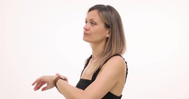 Kadın kol saatine bakar ve beyaz arka planda iş arkadaşını beklemeye devam eder. Siyah kolsuz bluzlu sarışın yoldaşını sabırsızlıkla bekliyor.