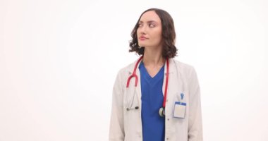 Üniformalı gülümseyen kadın doktor ellerini beyaz arka planda tutuyor. Neşeli yüz ifadesi olan kadın terapist işaret parmaklarıyla dikkat çekiyor.