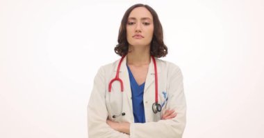 Beyaz önlüklü kadın doktor, beyaz arka planda güvensizlik göstererek başını sallıyor. Kolları göğsünde çapraz duran kadın terapist duygularını ifade ediyor.