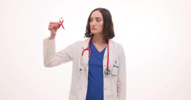 Kadın doktor beyaz arka planda kırmızı kurdele ve prezervatif gösteriyor. Üniformalı kadın doktor klinikteki hastalara HIV AIDS 'in önlenmesini hatırlatıyor