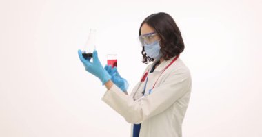 Koruyucu üniformalı kadın bilim adamı beyaz arka planda reaksiyonlar üzerinde çalışıyor. Kadın sıhhiyeci, deney tüplerindeki sıvıları incelemeye hazırlanıyor.