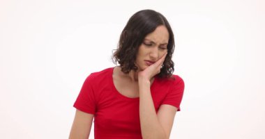 Genç bir kadın beyaz arka planda şiddetli diş ağrısı hissederek yüzüne dokunuyor. Esmer kadın diş problemleri yüzünden acı çekiyor.