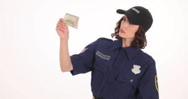 Polis memuru banknotu beyaz arka planda büyüteçle inceliyor. Memur, gerçekliği ve sahteleri doğrulamak için ayrıntıları analiz eder.