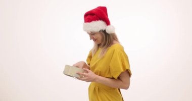 Şok olmuş Noel Baba şapkalı kadın Noel hediyesini beyaz arka planda açıyor. Mutlu sarışın kadın akıllı telefonu alıp lüks bir hediyeyle neşe ifade ediyor.