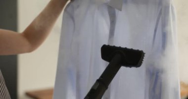 Kadınlar buluşmadan önce koca gömleği ütülemek için buhar cihazı kullanıyor. Özenli ev hanımı, hassas kumaş için özel ekipman kullanarak kırışıklıkları temizler.