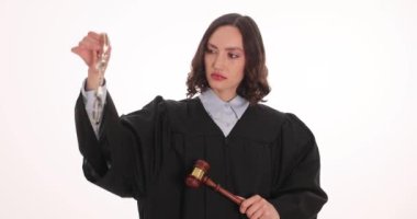 Kadın yargıç beyaz arka planda kelepçe ve tokmak tutuyor. Katı yüz ifadesi olan bir kadın nihai kararı açıklamaya hazırlanıyor.