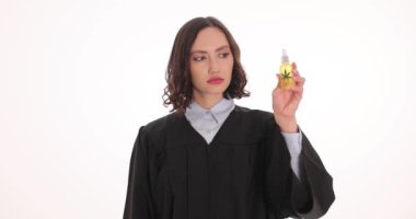 Kadın yargıç elinde beyaz arka planda kelepçe gösteren bir şişe CBD yağı tutuyor. Esrar mevzuatını çevreleyen hukuki güçlükler kavramı