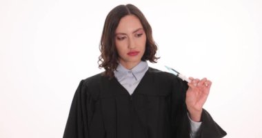 Kadın yargıç beyaz arka planda uyuşturucu ve kelepçeli şırınga gösteriyor. Siyah elbiseli esmer kadın mahkeme salonunda nihai karar için hazırlanıyor.