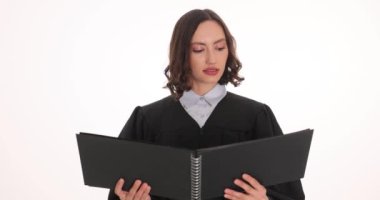 Siyah elbiseli kadın avukat kapanış argümanını beyaz duvara karşı tutarken okuyor. Ciddi yüz ifadesi olan bir kadın olayı araştırıyor.