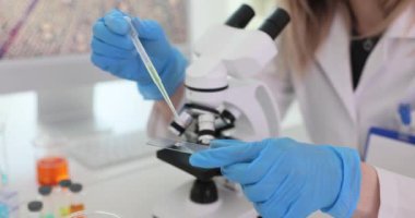 Laboratuvar çalışanı, iş yerindeki pipetle cam kaydırağın üzerine örnek döküyor. Dişi, numuneyi mikroskop altında incelemeye hazırlar.