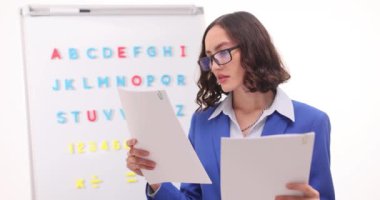 Ciddi kadın öğretmen belgeleri titizlikle gözden geçirir. Genç pedagog çalışmaları İngiliz alfabesi yakınlarındaki tutarsızlıkları kontrol eden kağıtların içeriği