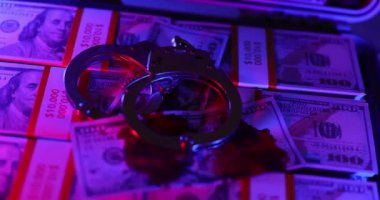 Kelepçeler loş ışıkta parıldıyor ve bir tomar banknotun üzerinde yatıyor. Çelik kelepçeler mali suç ve açgözlülüğün olası sonuçlarını simgeler.