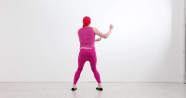 Canlı pembe kıyafetli erkek dansçı stüdyoda modern dans rutinini prova ediyor. Fitness antrenörü sanatsal ifade ve komik hareket yavaş çekim gösterir