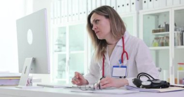 Evrak işleriyle uğraşan olumlu kadın doktor hastane ofisindeki bilgisayara bakıyor. Kadın doktor klinikteki online randevu verilerini kontrol eden raporlar yazıyor