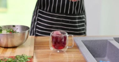Kadın modern mutfakta şeffaf kupaya rafine şeker küpü dökerek amber çayı demliyor. Hanımlar içeceklerin tadını yavaş çekimde çıkarırlar.