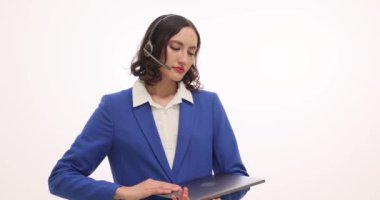 Yorgun kadın, elinde dizüstü bilgisayarla beyaz arka planda kulaklığı çıkartıyor. Kadın müşteri yöneticisi ağır çekimde çalıştıktan sonra yoruluyor.